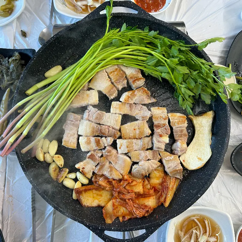 불판 위에서 익어가는 삼겹살과 미나리, 김치