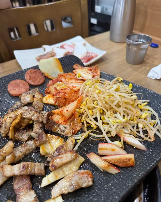 불판 위에서 지글거리는 김치, 콩나물, 그리고 구워진 대패 삼겹살