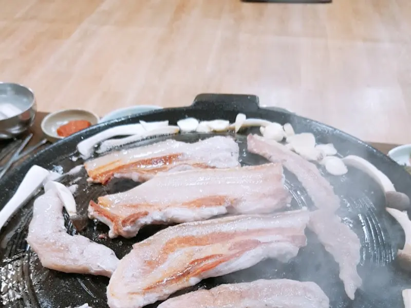 솥뚜껑에 삼겹살, 김치, 버섯, 마늘이 구워지고 있는 모습