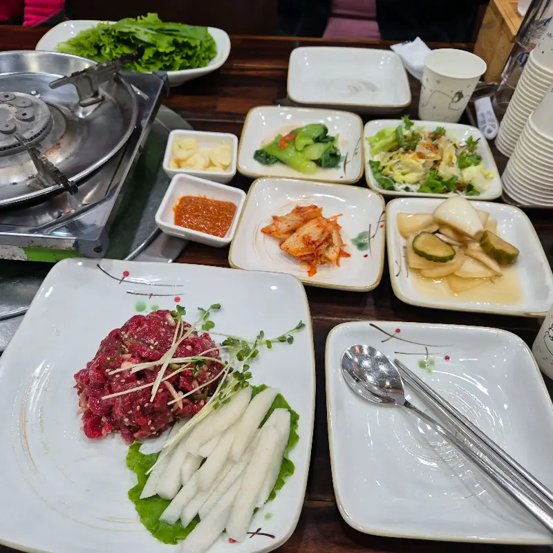 육회 비빔밥과 각종 반찬이 차려진 테이블 사진