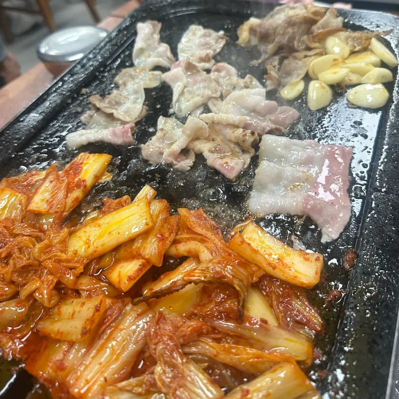 불판 위에서 익어가는 삼겹살, 김치, 마늘