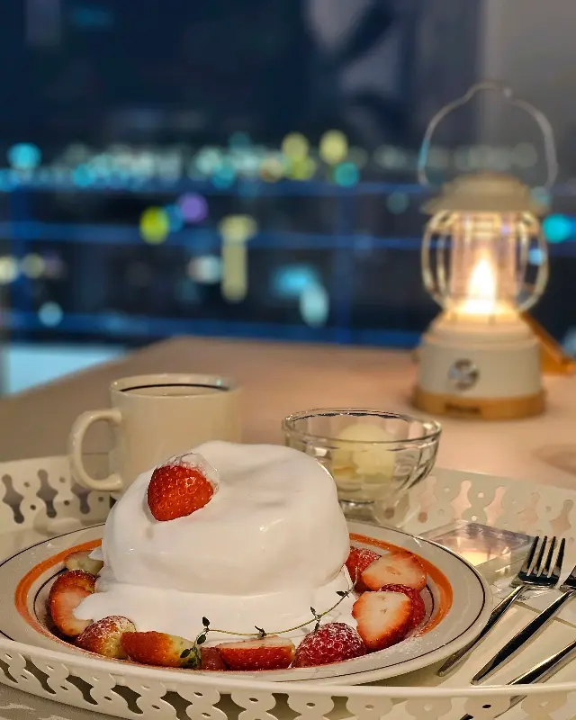 테이블 위에 놓인 딸기 수플레와 커피, 그리고 야경을 담은 카페 파로스의 사진