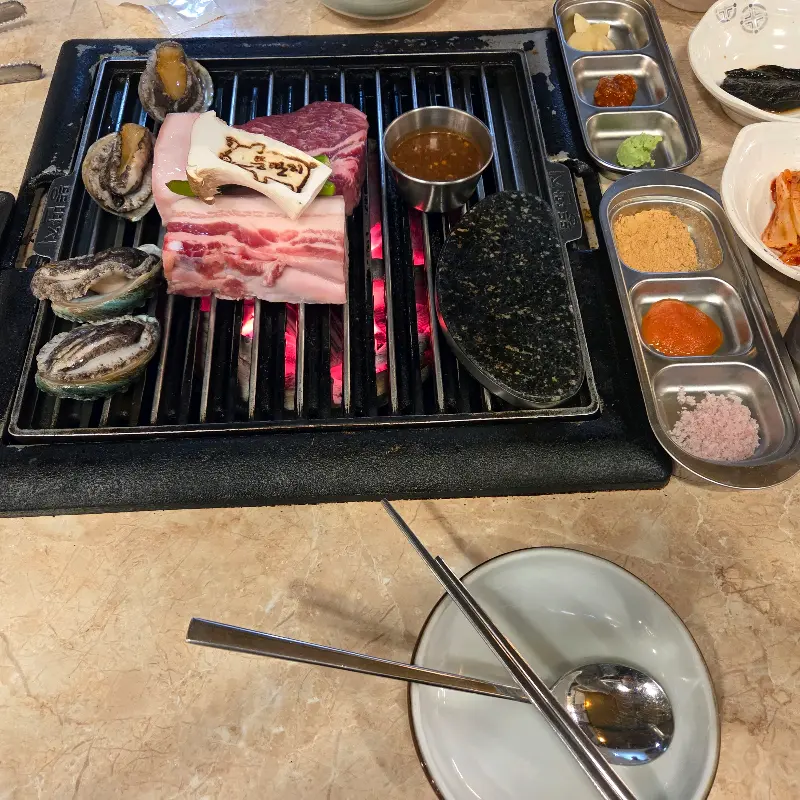 불판 위에서 흑돼지, 전복, 버섯이 맛있게 구워지고 있는 모습