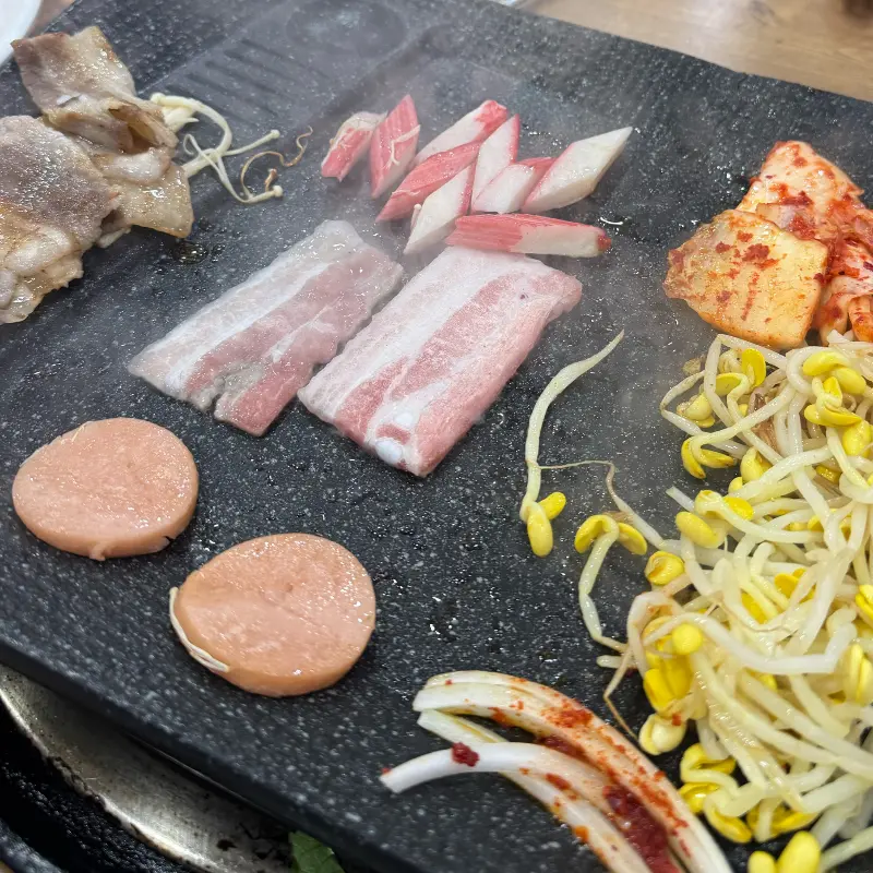 불판 위에서 익어가는 햄, 김치, 콩나물과 대패삼겹살