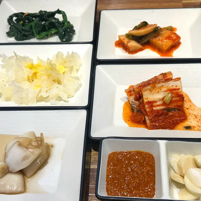 다양한 종류의 밑반찬들이 깔끔하게 담겨 테이블에 놓여있다.