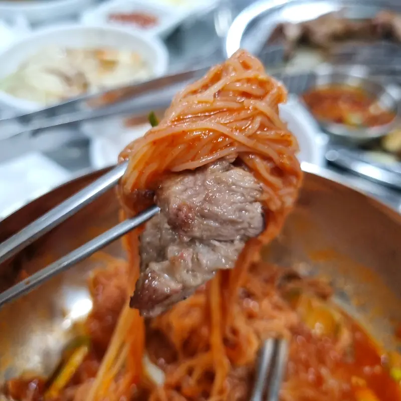 젓가락으로 비빔국수와 고기를 함께 집은 모습