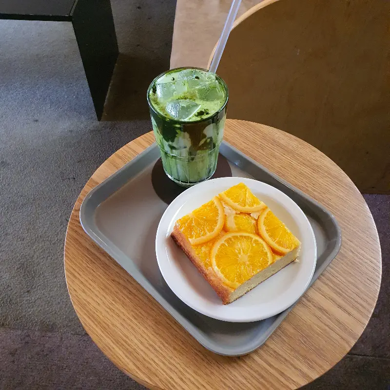 테이블 위에 놓인 청량한 말차 음료와 오렌지 조각이 올라간 케이크