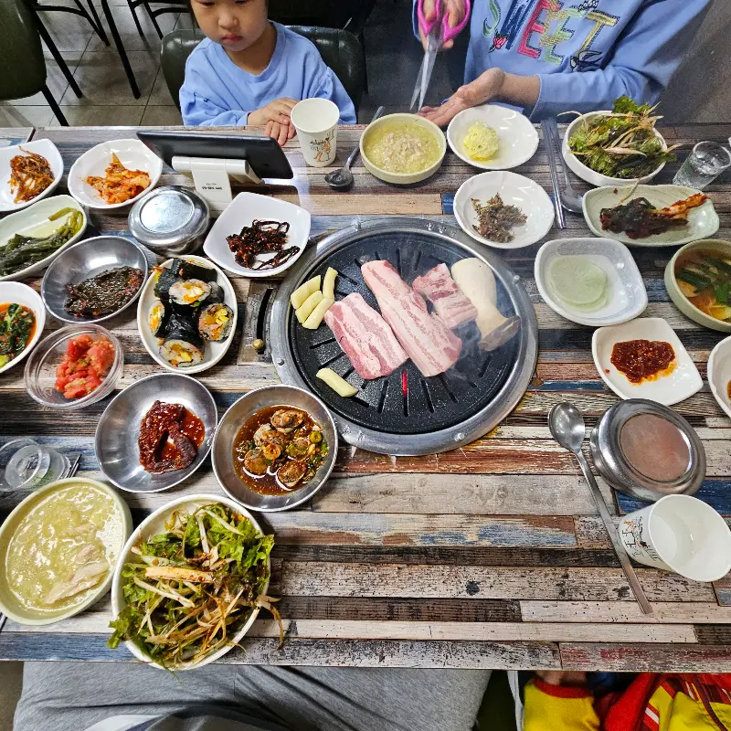 푸짐하게 차려진 밑반찬과 고기 불판이 놓인 테이블 전경