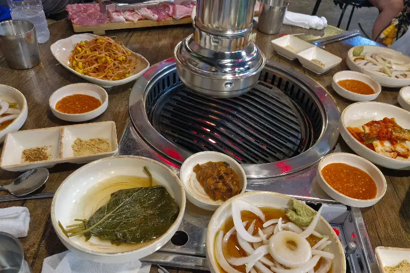 불판 위의 고기와 다양한 곁들임 찬들