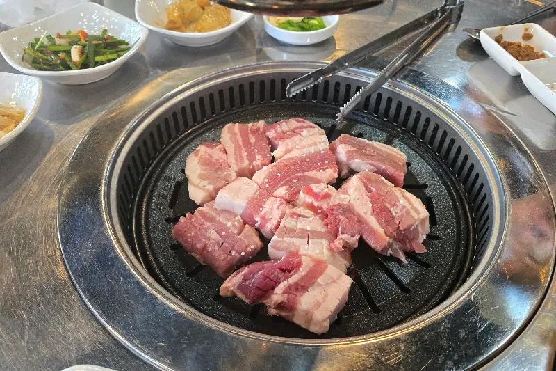 불판 가득 채운 삼겹살과 곁들임 야채