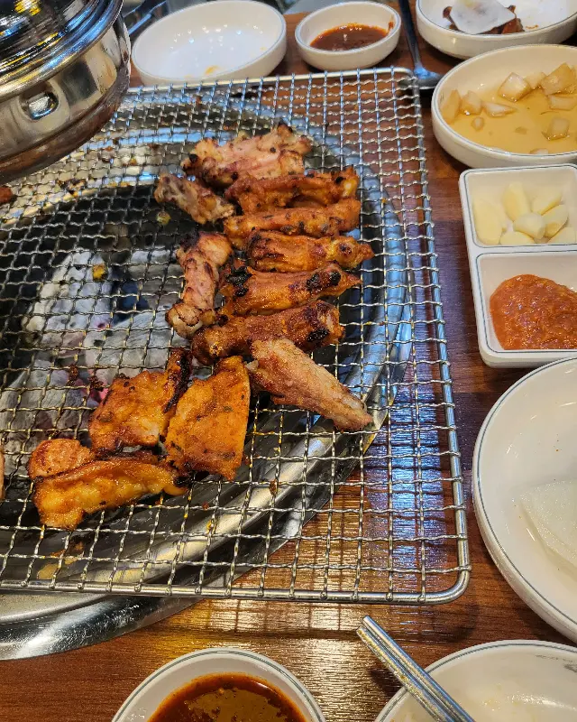 숯불 위에서 맛있게 익어가는 닭갈비와 다양한 밑반찬들