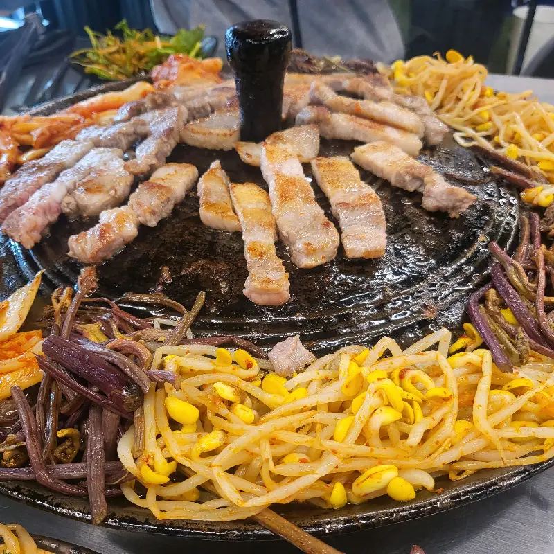 솥뚜껑 가득 올려진 삼겹살과 각종 채소