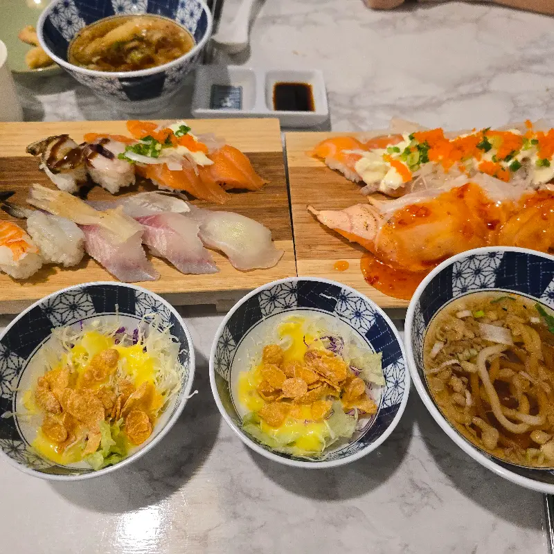 다양한 종류의 초밥과 샐러드, 우동이 놓여있는 테이블