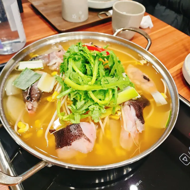 아구지리가 테이블 위 버너에 올려져 끓고 있는 모습. 쑥갓이 듬뿍 올라가 있고, 국물이 맑다.