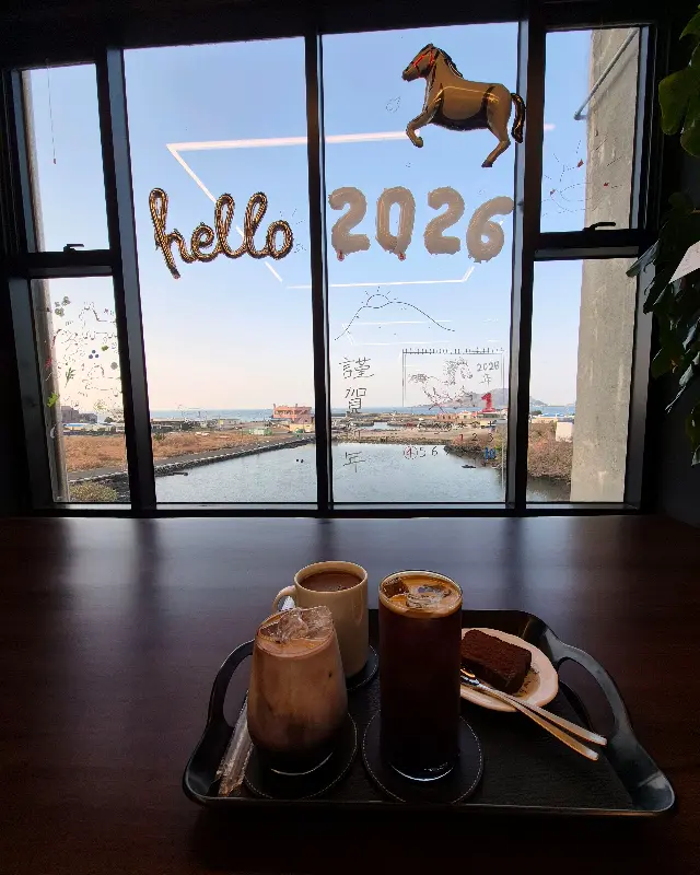 테이블 위에 놓인 음료와 디저트, 그리고 창밖의 바다 풍경