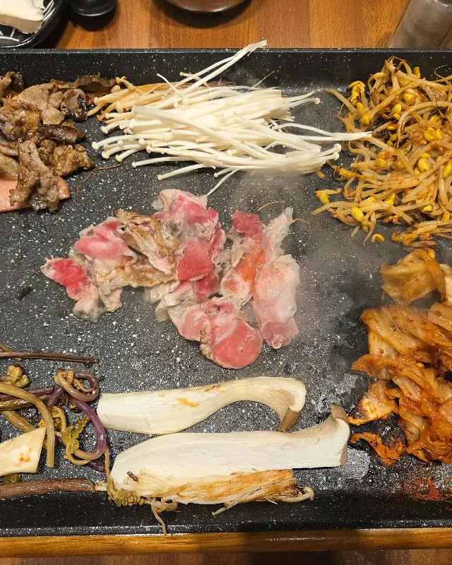 불판 가득 구워진 고기와 김치, 콩나물, 버섯