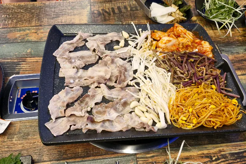 불판 위에 올려진 고기와 김치, 콩나물