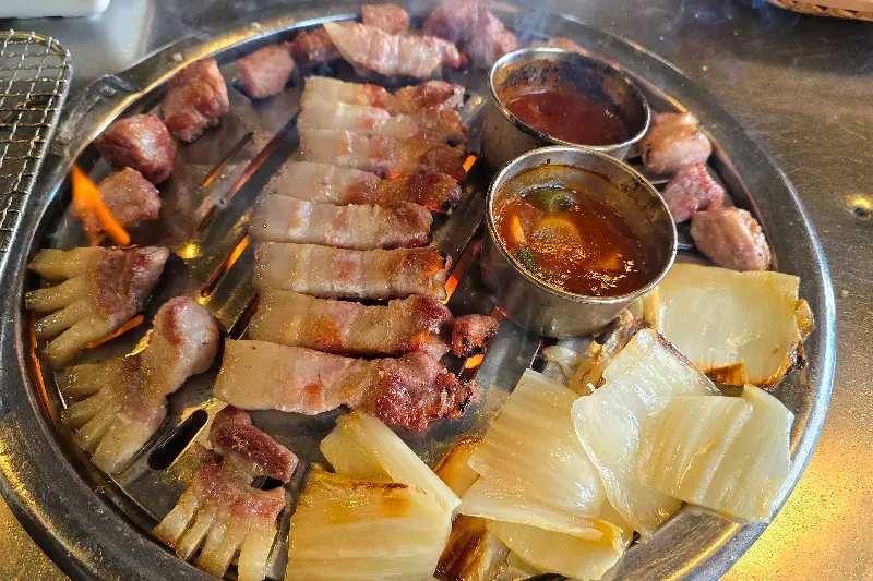 다양한 부위의 흑돼지와 백김치가 불판 위에 올려져 있다.
