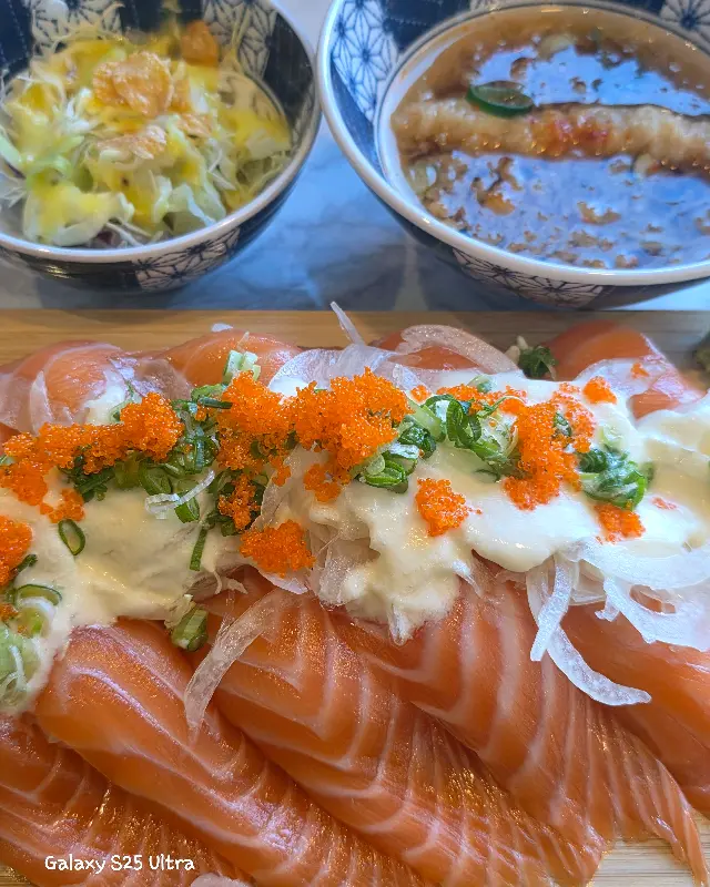 윤기가 흐르는 연어 초밥 위에 소스와 토핑이 얹어진 모습