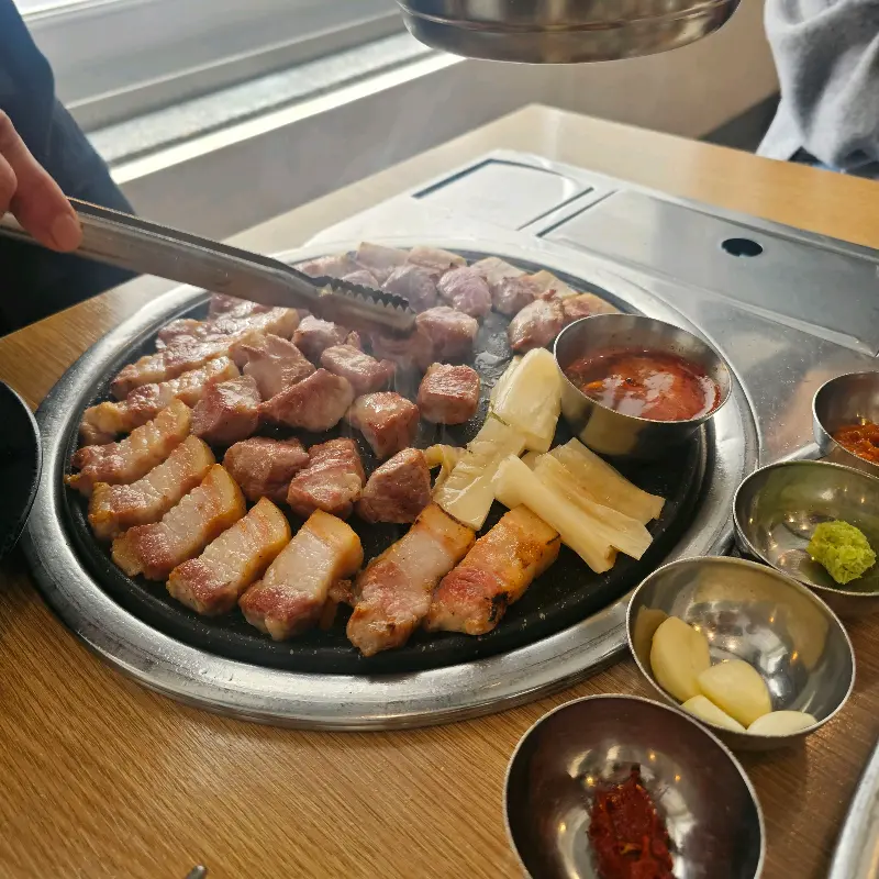 불판 위에서 흑돼지, 멜젓, 백김치가 함께 구워지는 모습