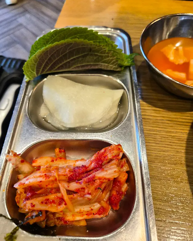 깻잎, 쌈무, 김치가 담겨 있는 반찬 접시