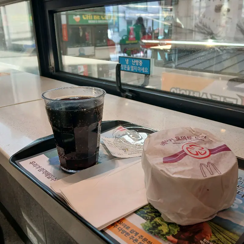 창가 테이블에 놓인 버거와 콜라