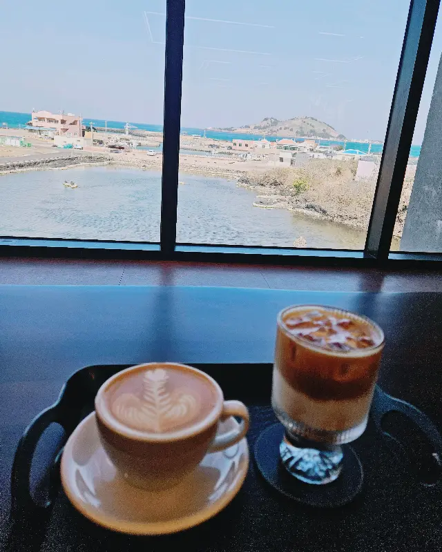 창밖의 비양도 바다 뷰와 함께 놓인 라떼와 음료