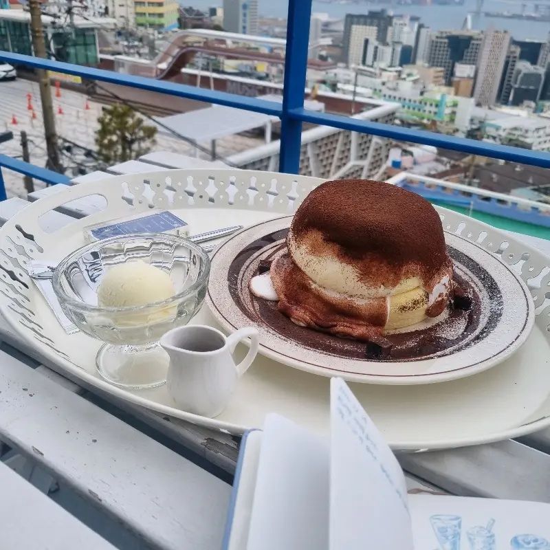 테이블에 놓인 티라미수 수플레, 아이스크림, 커피, 그리고 부산 시내 뷰를 담은 카페 파로스의 사진