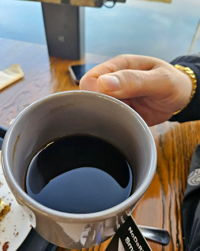 테이블 위에 놓인 커피잔. 잔 안에는 검은 액체가 담겨 있고, 주변에는 냅킨과 스푼이 놓여 있다.