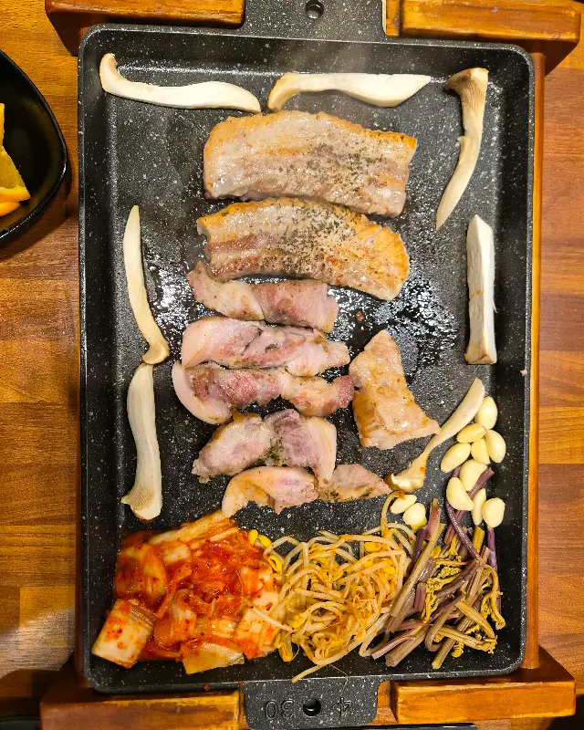 불판 위에 구워진 삼겹살, 김치, 버섯, 콩나물