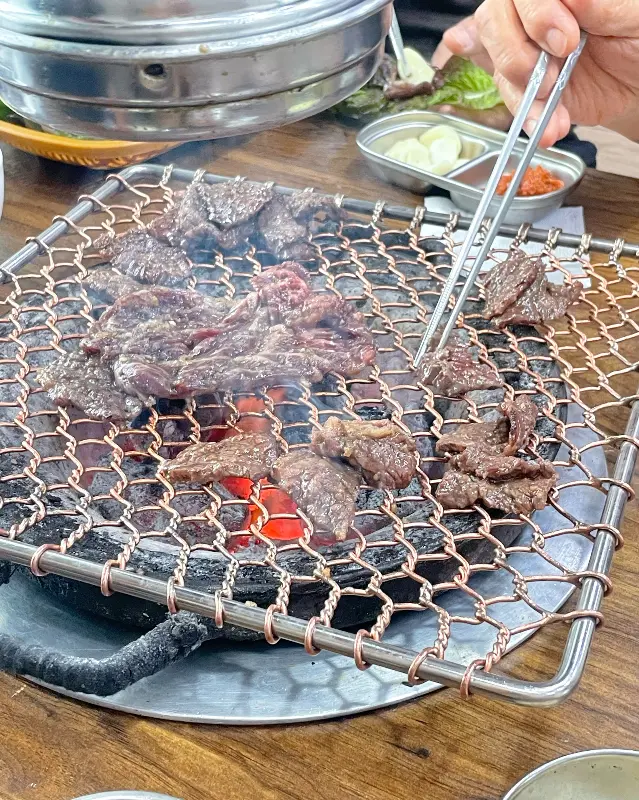 숯불 위에서 구워지는 고기를 집게로 뒤집는 모습