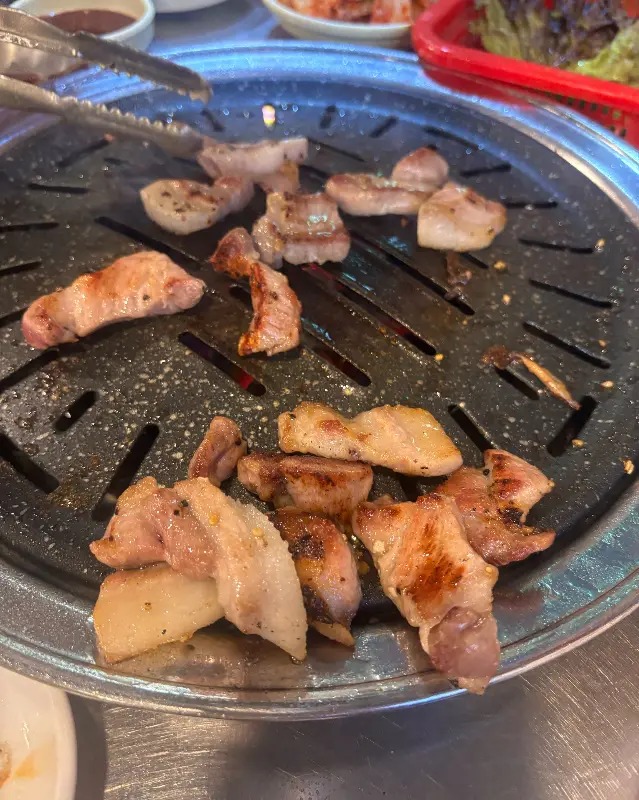 불판 위에서 익어가는 삼겹살과 돼지 꼬리