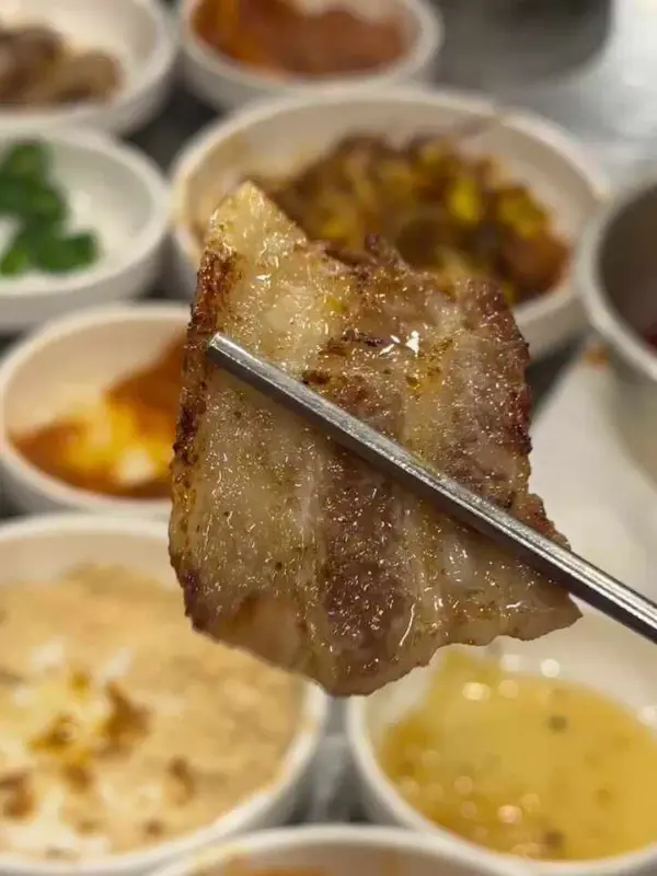 노릇하게 구워진 삼겹살 한 점을 젓가락으로 들어올리는 모습