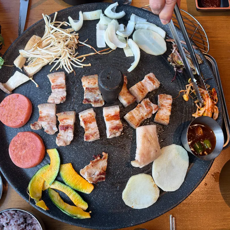 잘 구워진 삼겹살과 다양한 채소를 곁들여 먹음직스럽게 쌈을 싸는 모습