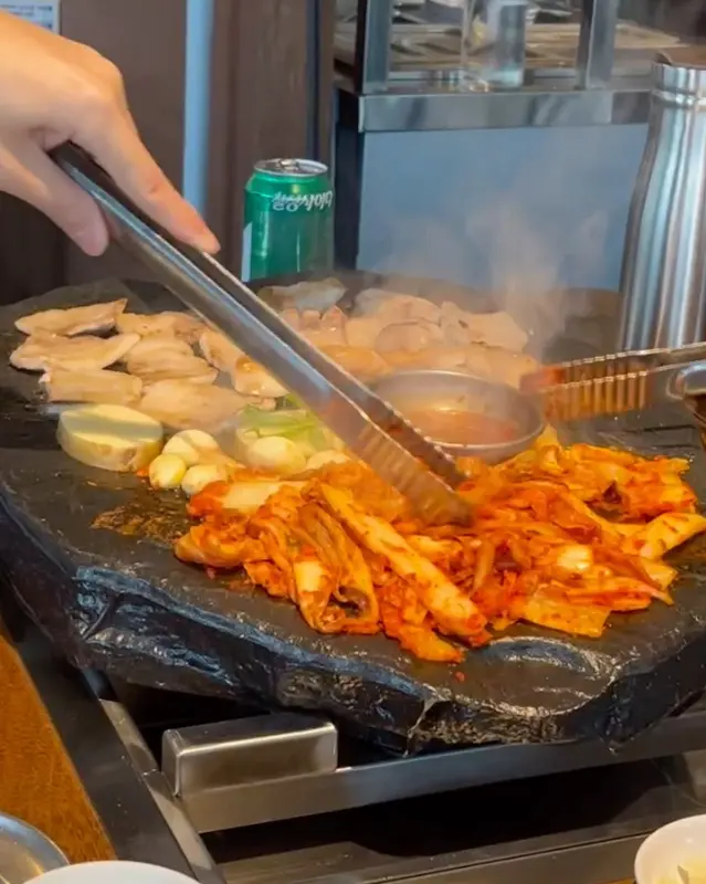 돌판 위에 김치, 마늘, 고기가 구워지는 모습