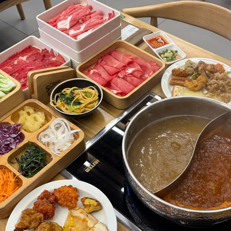 샤브샤브 냄비와 각종 채소, 고기, 사이드 메뉴가 놓인 테이블