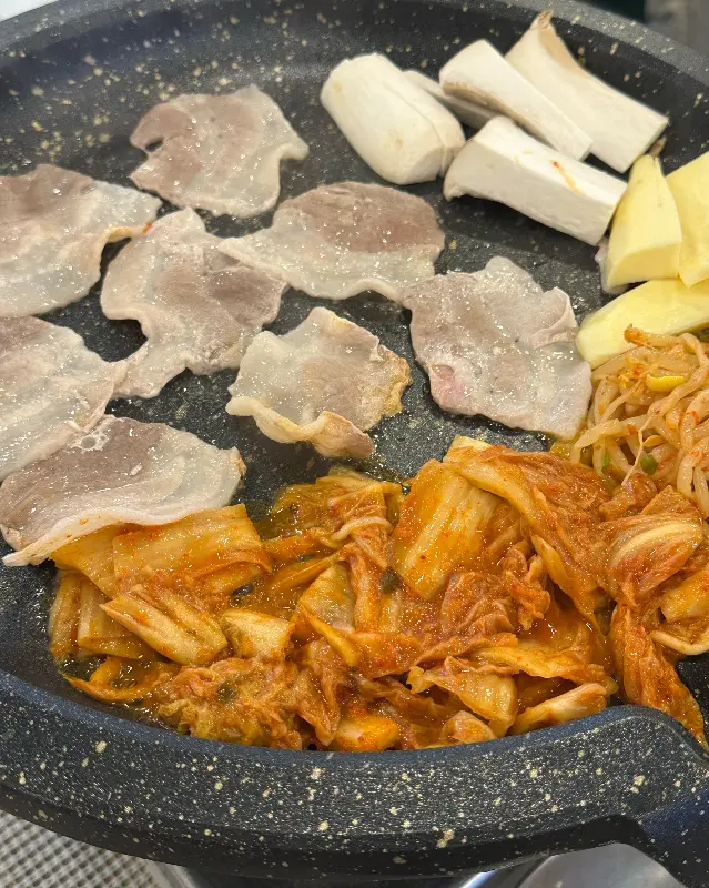 불판 위에서 익어가는 삼겹살, 김치, 버섯
