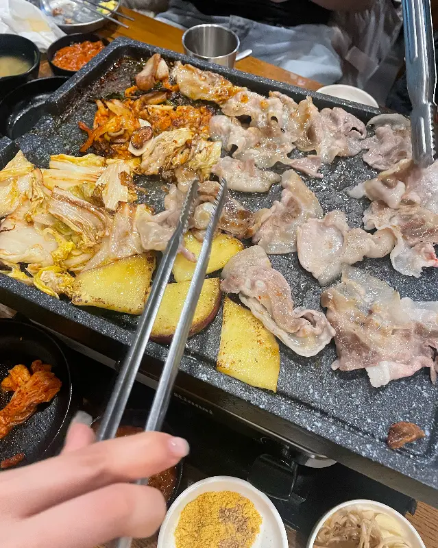 불판 위에서 익어가는 대패 삼겹살과 김치, 콩나물무침