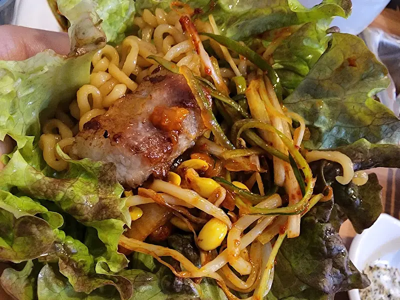 싱싱한 상추에 삼겹살, 콩나물, 파절이를 올려 쌈을 싸 먹는 모습