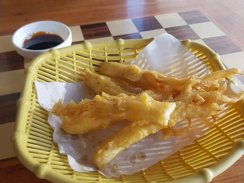 바삭하게 튀겨진 인삼 튀김이 노란색 바구니 접시에 담겨 있다. 옆에는 간장 종지가 놓여 있다.