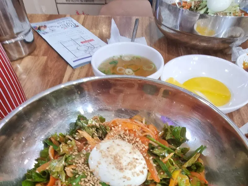 테이블 위에 놓인 비빔국수. 맑은 멸치 육수와 노란 단무지가 함께 보인다.