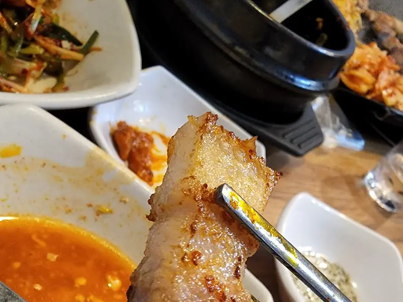 잘 구워진 삼겹살 한 점을 젓가락으로 집어 올린 모습