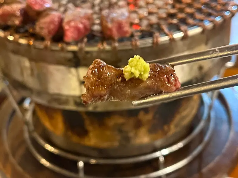 잘 익은 한우 위에 와사비를 살짝 올려 젓가락으로 집어 올린 클로즈업 샷