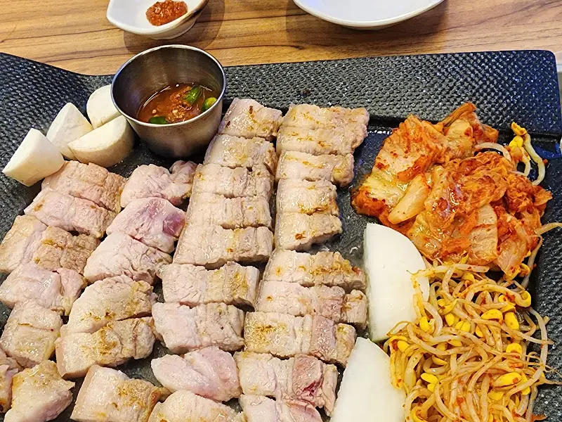 잘 구워진 삼겹살과 김치, 콩나물이 불판 위에 놓여 있는 모습