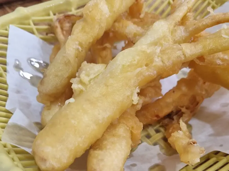 노란색 플라스틱 바구니 접시에 튀김이 담겨 있고, 인삼 튀김의 겉면이 클로즈업 되어 있다.