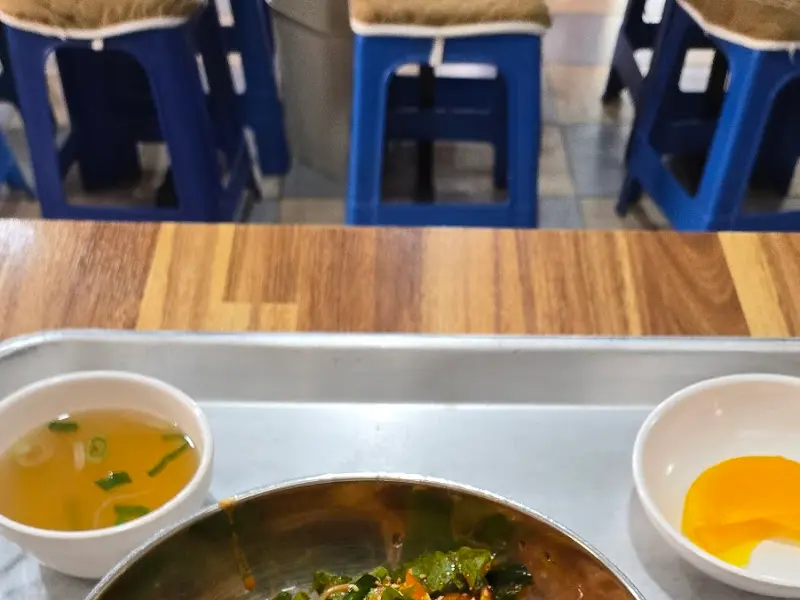 테이블 위에 놓인 비빔국수. 곁들여 나오는 맑은 국물과 노란 단무지가 함께 보인다.