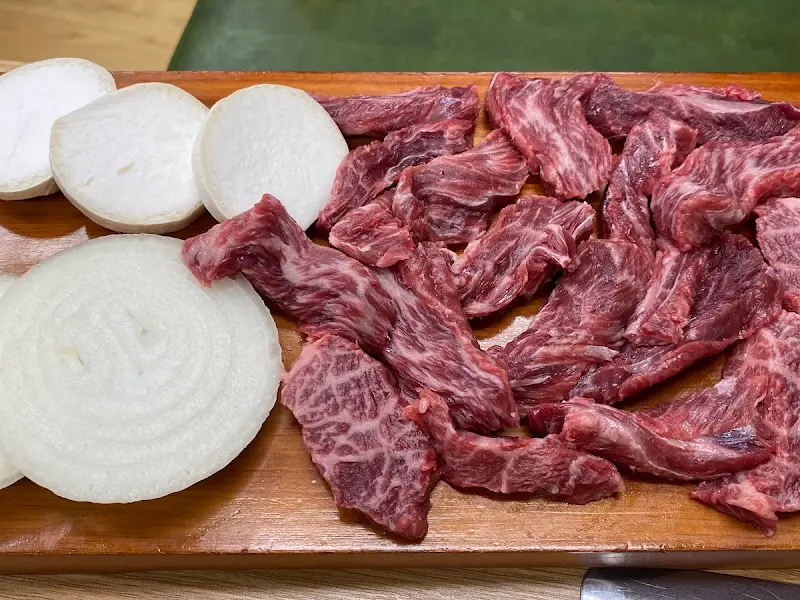 나무 도마 위에 가지런히 놓인 한우 모듬. 곁들여 먹을 양파도 보인다.