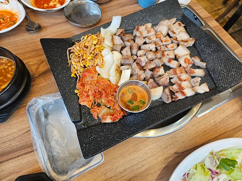 불판 위에 구워진 삼겹살, 김치, 콩나물, 양파의 모습