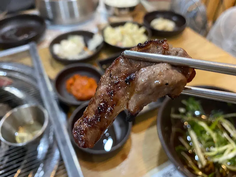 윤기가 흐르는 구워진 소고기를 젓가락으로 집는 모습