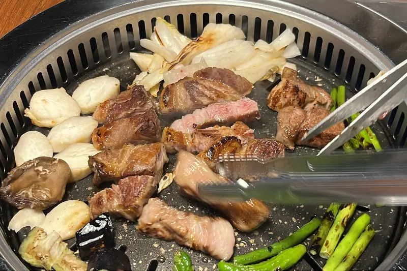 불판 위에서 목살과 각종 채소가 함께 구워지는 모습